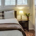 View into bedroom with light gray walls, floral carpeting, white bedding, and dark wooden nightstand