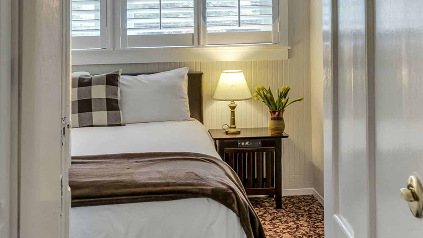 View into bedroom with light gray walls, floral carpeting, white bedding, and dark wooden nightstand