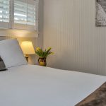 Bedroom with light gray walls, white bedding, and nightstand with lamp and vase of yellow tulips