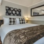 Bedroom with white walls, light gray wainscotting, floral carpeting, white bedding, and dark wooden nightstands