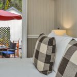 Bedroom with white walls, light gray wainscotting, white bedding, and view out to patio