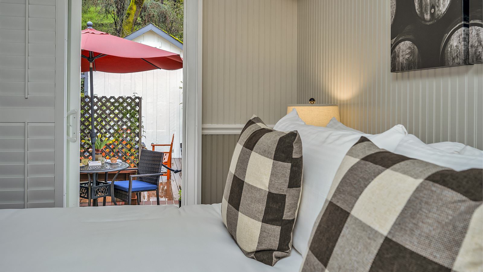 Bedroom with white walls, light gray wainscotting, white bedding, and view out to patio