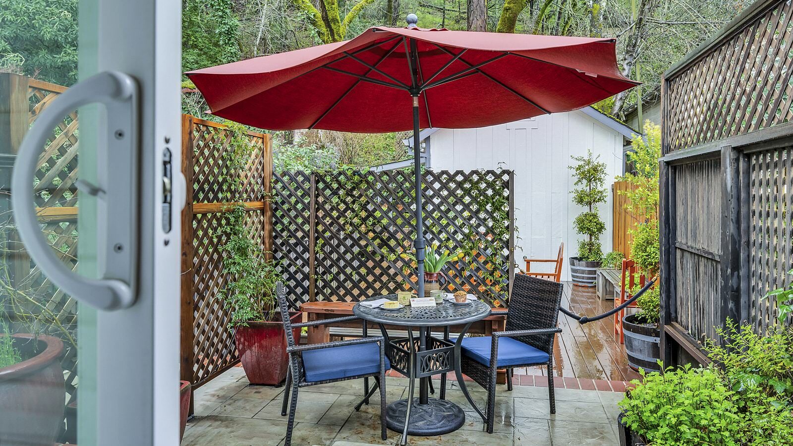 Back patio with metal patio dining table, dark wicker patio dining chairs, and red umbrella