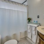 Bathroom with light gray walls, tub and shower combo, white toilet, and wooden vanity with light cream counter