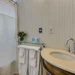 Bathroom with light gray walls, tub and shower combo, white toilet, and wooden vanity with light cream counter