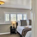 View into bedroom with white walls, light gray wainscotting, light colored carpeting, white bedding, and dark wooden nightstands