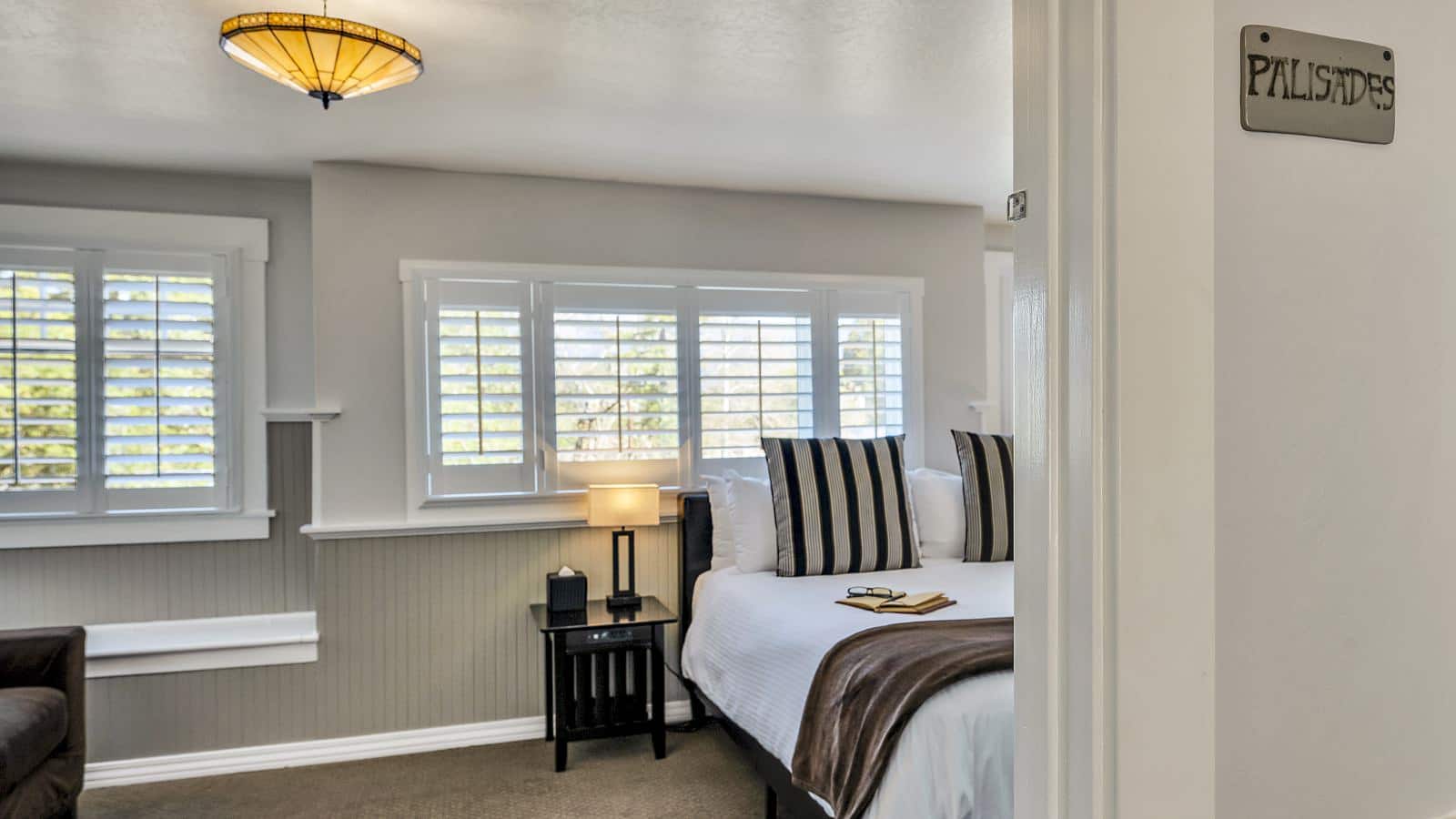 View into bedroom with white walls, light gray wainscotting, light colored carpeting, white bedding, and dark wooden nightstands