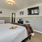 Bedroom with white walls, light gray wainscotting, light colored carpeting, white bedding, and dark wooden nightstands