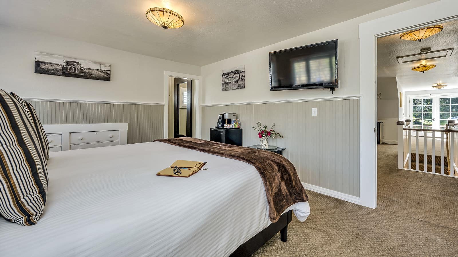 Bedroom with white walls, light gray wainscotting, light colored carpeting, white bedding, and dark wooden nightstands