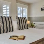 Bedroom with white walls, light gray wainscotting, white bedding, and in-wall white dresser drawers
