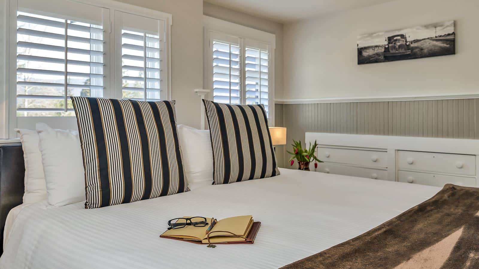 Bedroom with white walls, light gray wainscotting, white bedding, and in-wall white dresser drawers