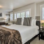 Bedroom with white walls, light gray wainscotting, light colored carpeting, white bedding, and dark wooden nightstands