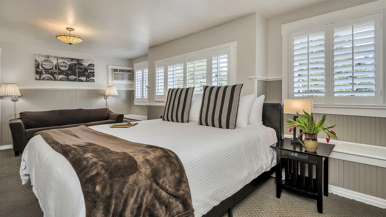 Bedroom with white walls, light gray wainscotting, light colored carpeting, white bedding, and dark wooden nightstands