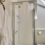 Bathroom with white walls, light gray wainscotting, and white tiled stand up shower