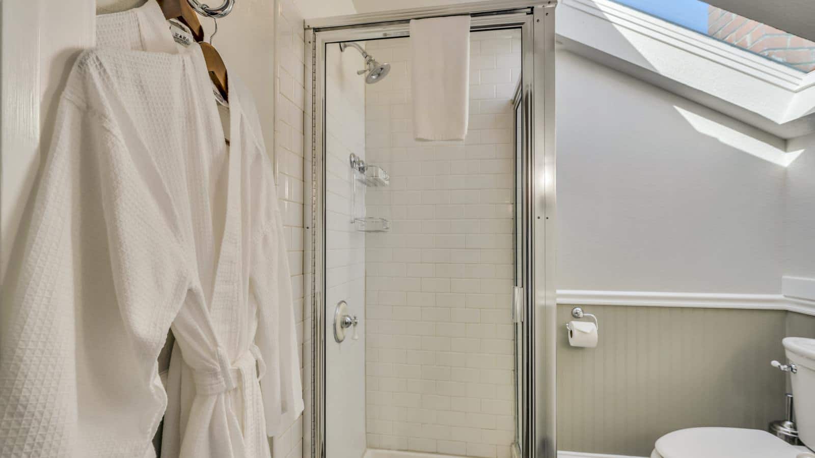 Bathroom with white walls, light gray wainscotting, and white tiled stand up shower