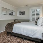 Bedroom with white walls, light gray wainscotting, floral carpeting, white bedding, and dark wooden nightstands