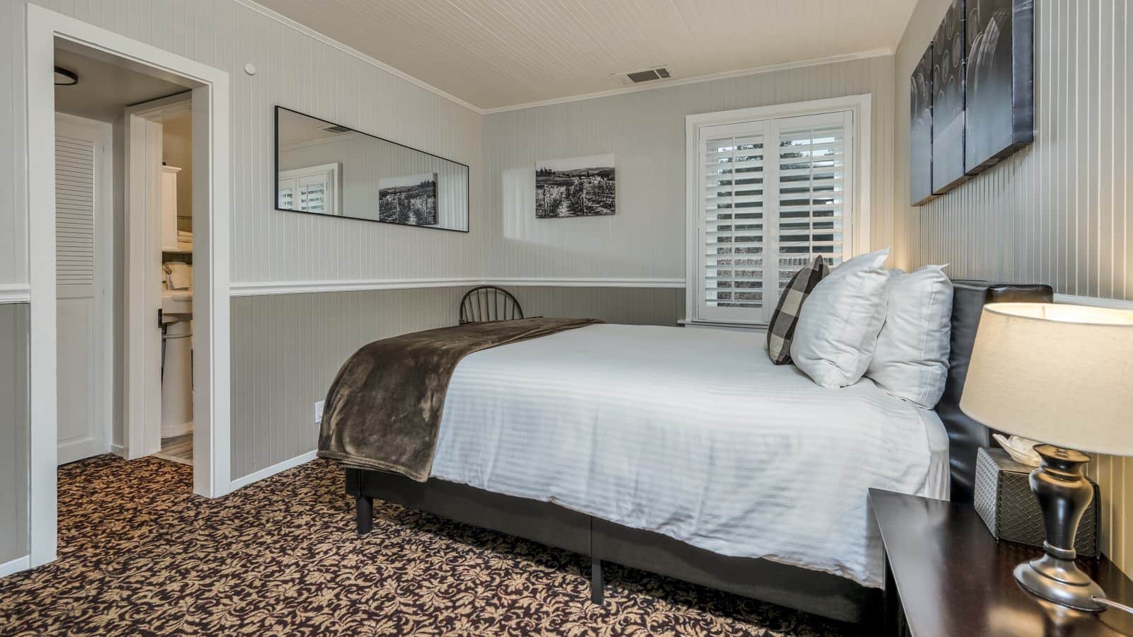Bedroom with white walls, light gray wainscotting, floral carpeting, white bedding, and dark wooden nightstands