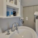 Close up view of white sink, white medicine cabinet, and towel bar with white towels