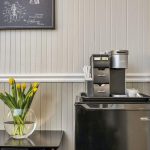 Close up view of black mini fridge with Keurig on top and black table with glass vase with yellow tulips