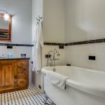 Bathroom with white walls, black and white tiled floor, dark wooden vanity, and white clawfoot tub