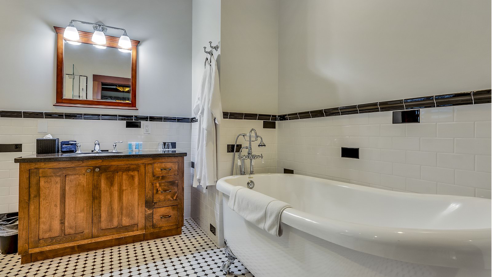 Bathroom with white walls, black and white tiled floor, dark wooden vanity, and white clawfoot tub