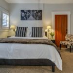 Bedroom with white walls, light colored carpeting, white bedding, black mini fridge, and dark wooden nightstands