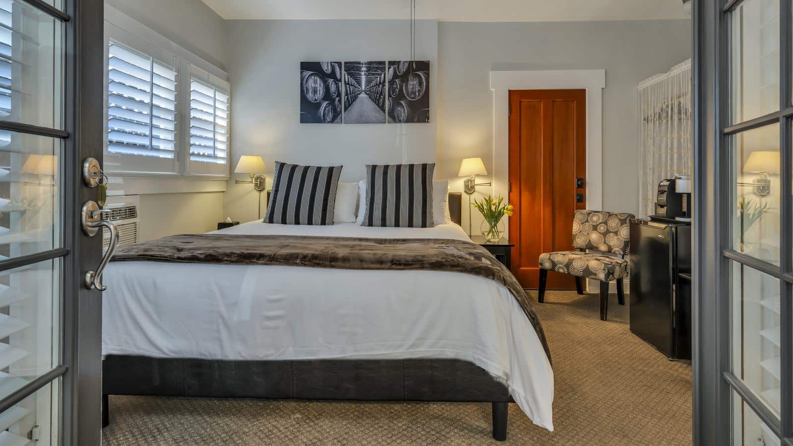 Bedroom with white walls, light colored carpeting, white bedding, black mini fridge, and dark wooden nightstands