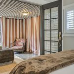 View from bedroom of back wooden deck with brown wicker patio furniture, lattice cover, and white and brown striped curtains
