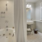Bathroom with white walls, light gray wainscotting, black and white tiled flooring, white tiled shower and tub combo, and white sink