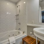 Bathroom with white walls, light gray wainscotting, white tiled shower and tub combo, and white sink