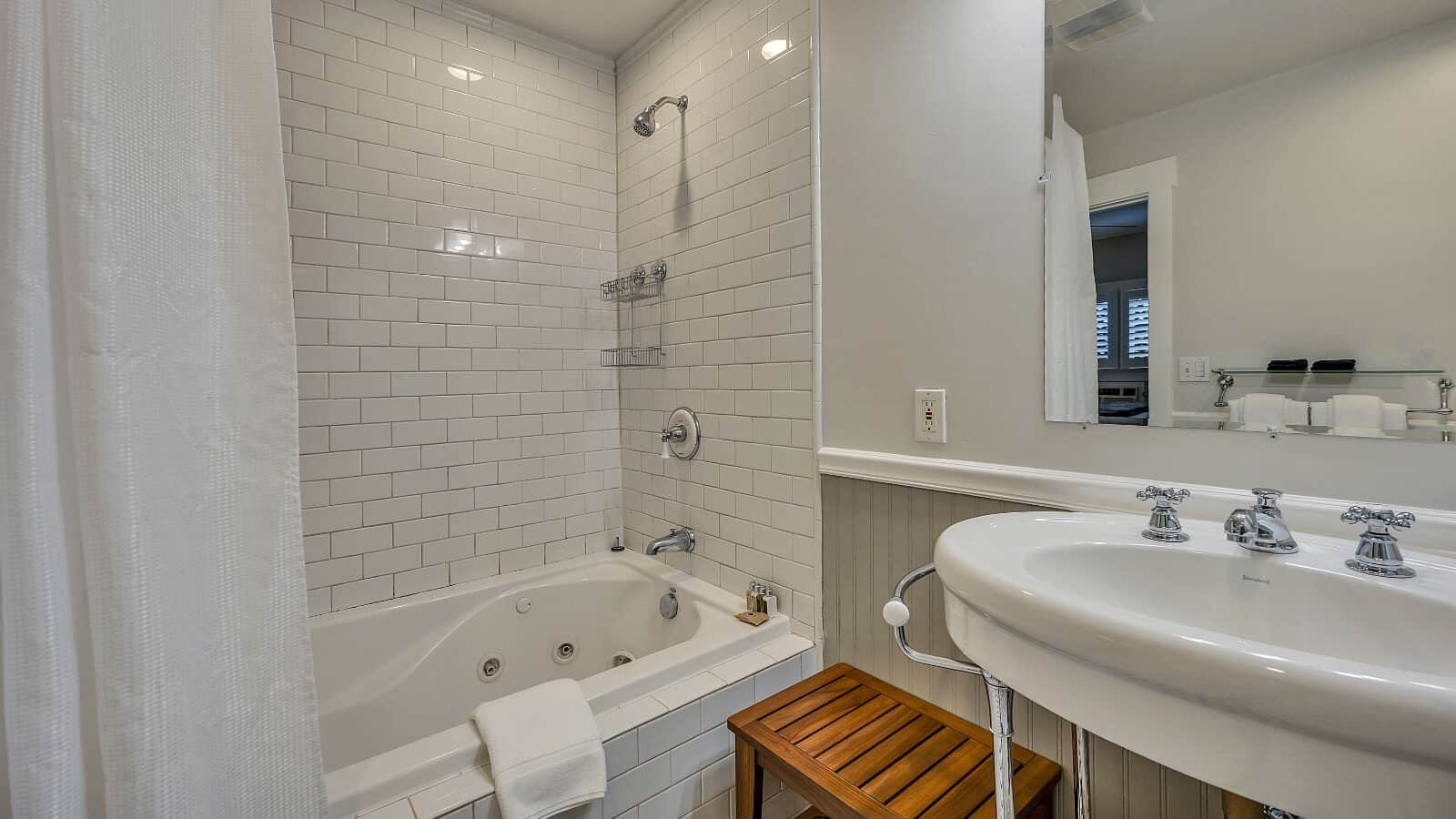 Bathroom with white walls, light gray wainscotting, white tiled shower and tub combo, and white sink
