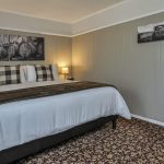 Bedroom with white walls, high light gray wainscotting, floral carpeting, white bedding, and dark wooden nightstands