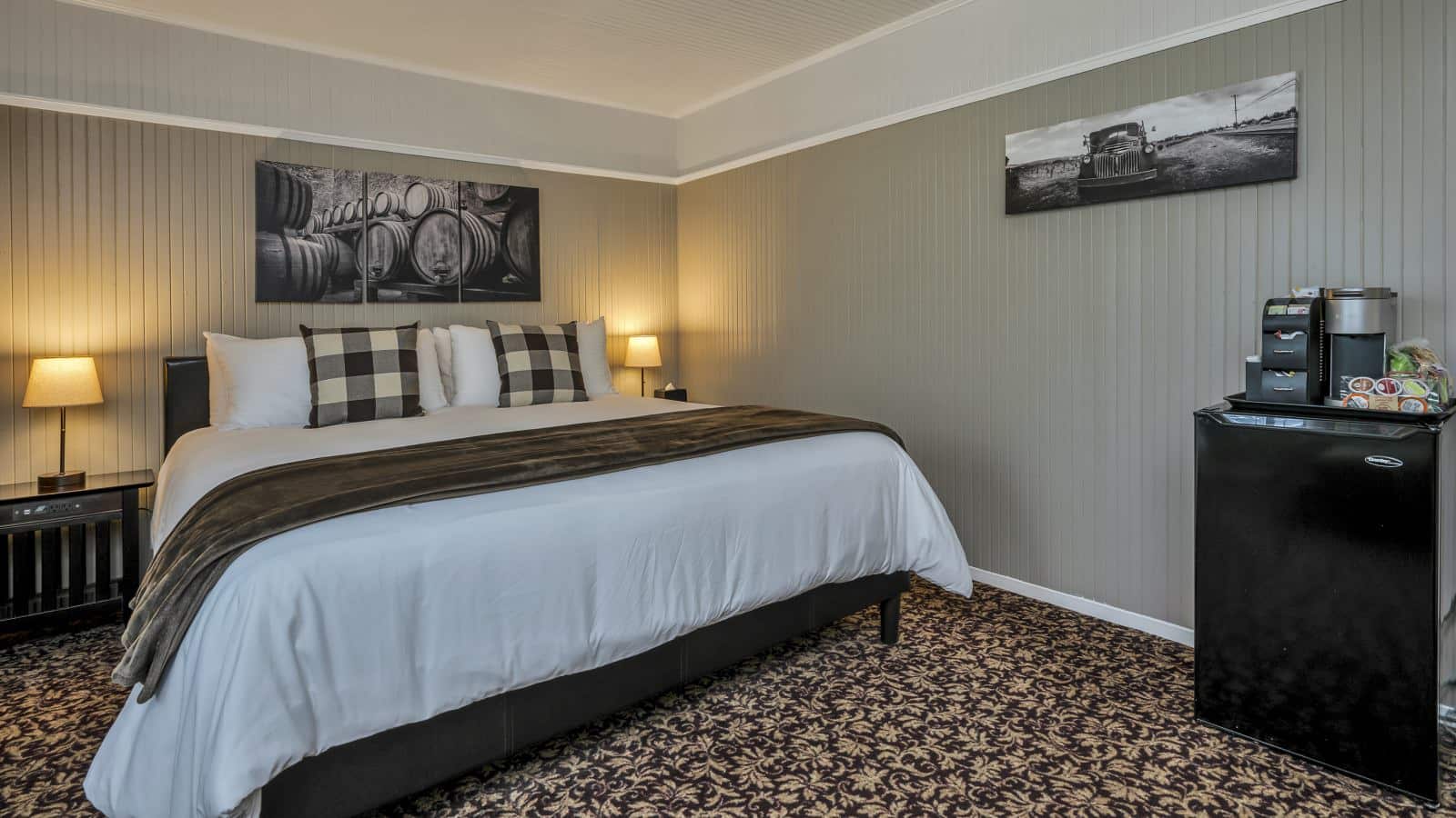 Bedroom with white walls, high light gray wainscotting, floral carpeting, white bedding, and dark wooden nightstands