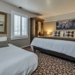 Bedroom with white walls, high light gray wainscotting, floral carpeting, white bedding, dark wooden armoire, and extra bed with white bedding