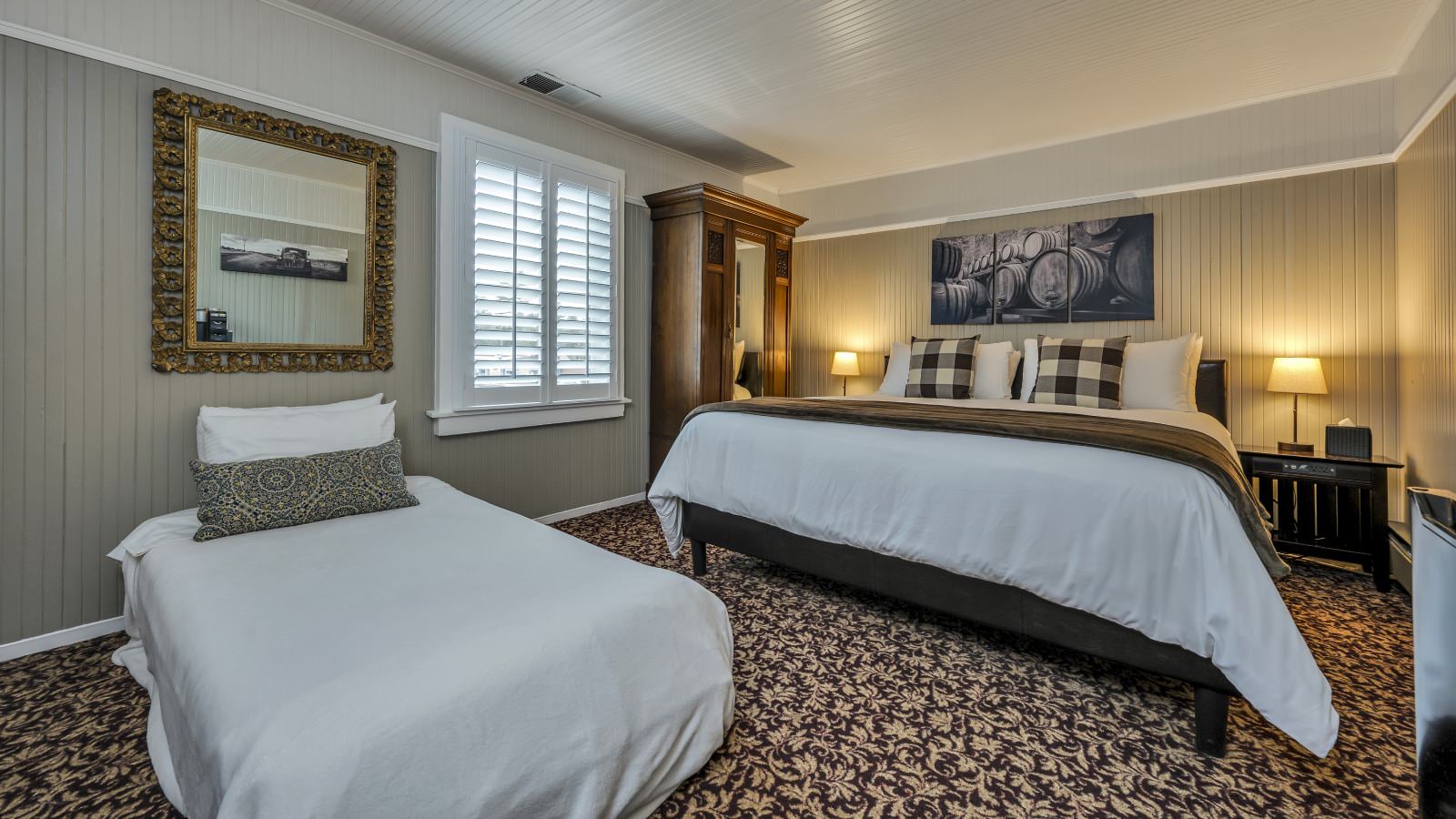 Bedroom with white walls, high light gray wainscotting, floral carpeting, white bedding, dark wooden armoire, and extra bed with white bedding