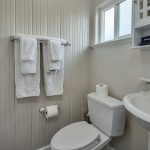 Bathroom with white walls, stand up shower, white toilet, and white sink