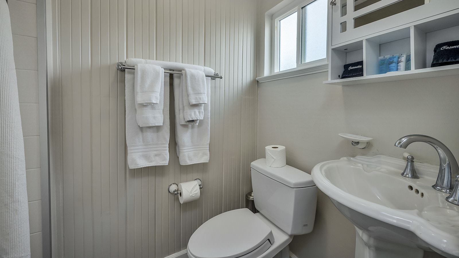 Bathroom with white walls, stand up shower, white toilet, and white sink
