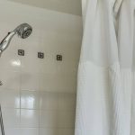 Close up view of stainless steel hand-held shower head in white tiled stand up shower