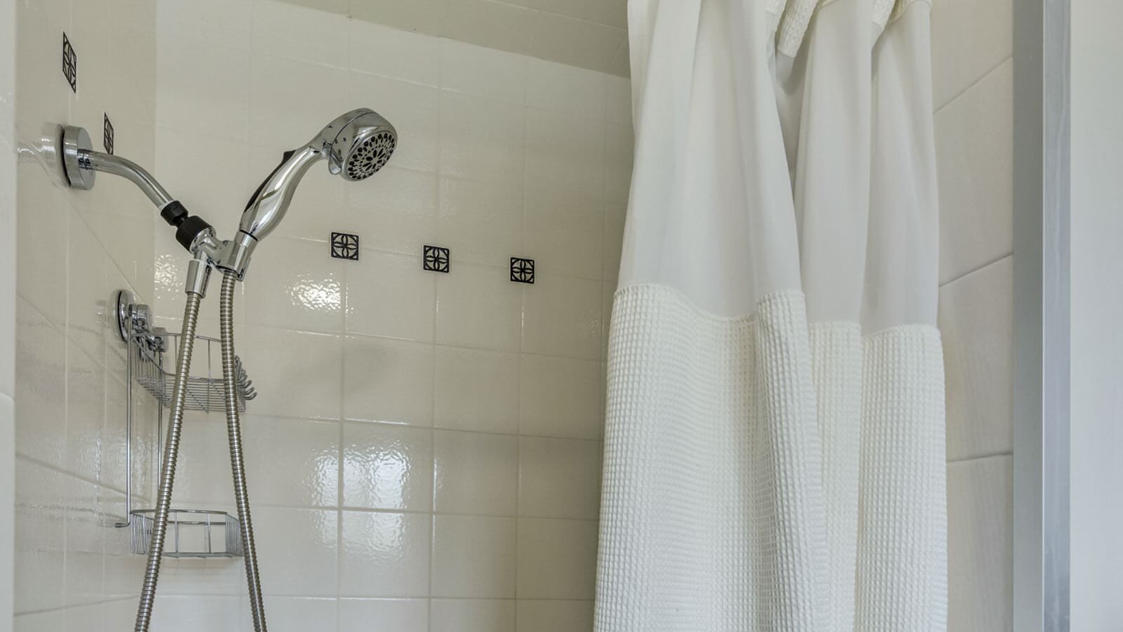 Close up view of stainless steel hand-held shower head in white tiled stand up shower
