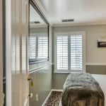 View into bedroom with white walls, light gray wainscotting, floral carpeting, and white bedding