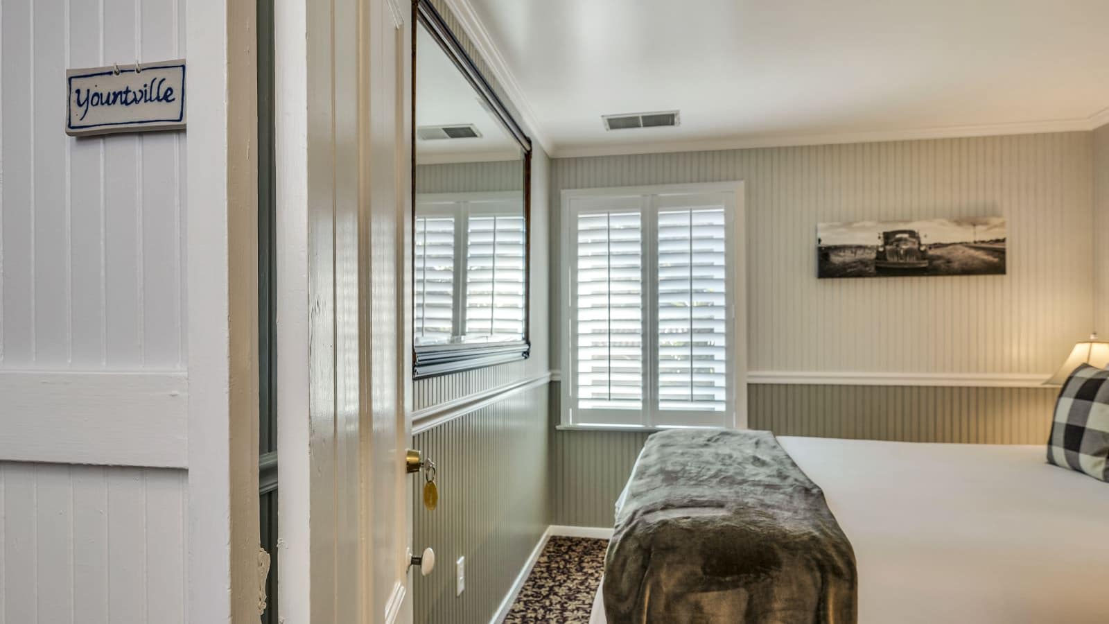 View into bedroom with white walls, light gray wainscotting, floral carpeting, and white bedding