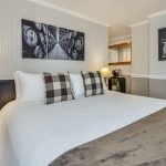 Bedroom with white walls, light gray wainscotting, floral carpeting, white bedding, and dark wooden nightstands
