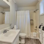Bathroom with white walls, tub and shower combo, white toilet, and white vanity