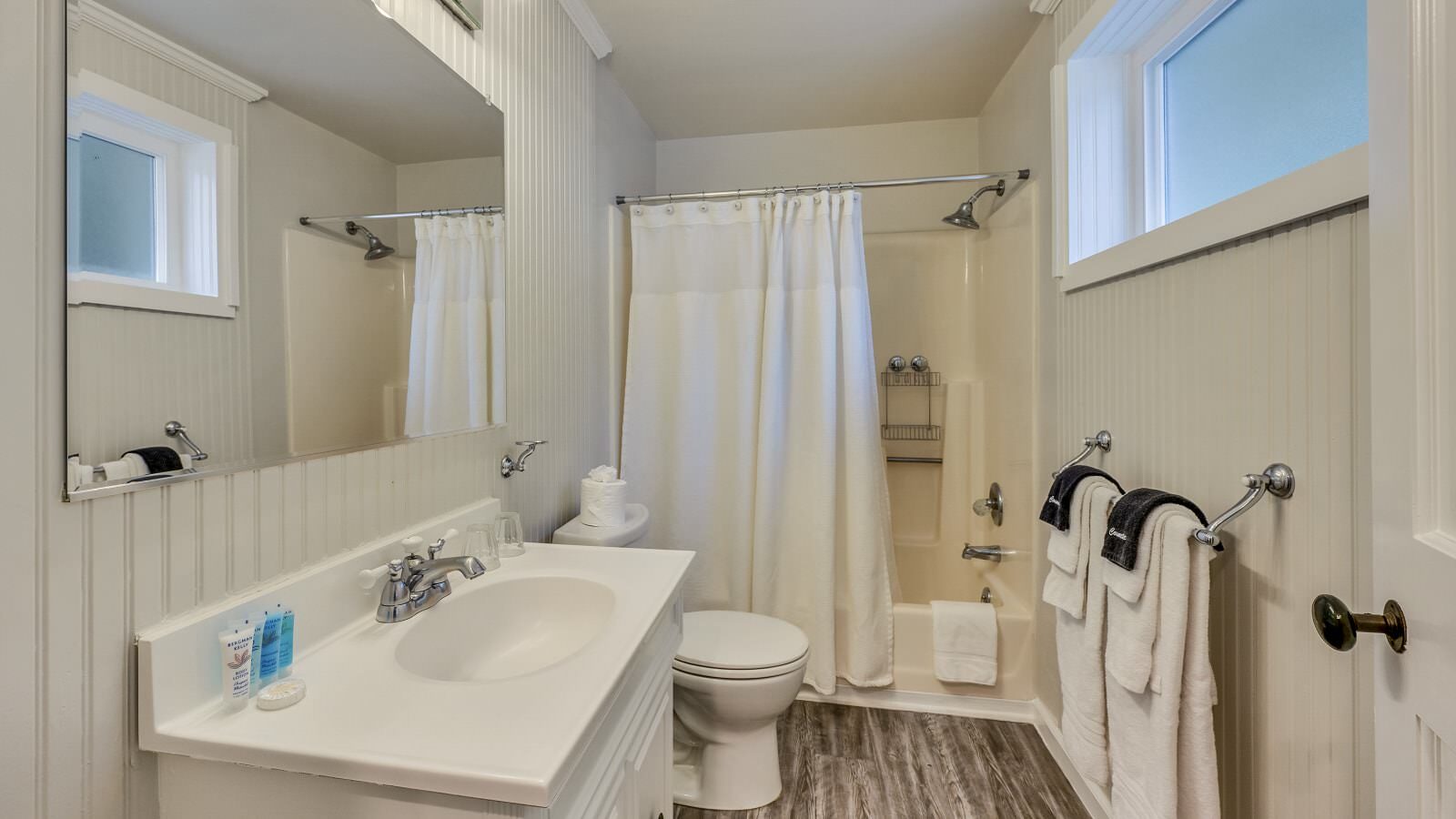 Bathroom with white walls, tub and shower combo, white toilet, and white vanity