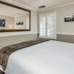 Bedroom with white walls, light gray wainscotting, floral carpeting, white bedding, and large framed mirror