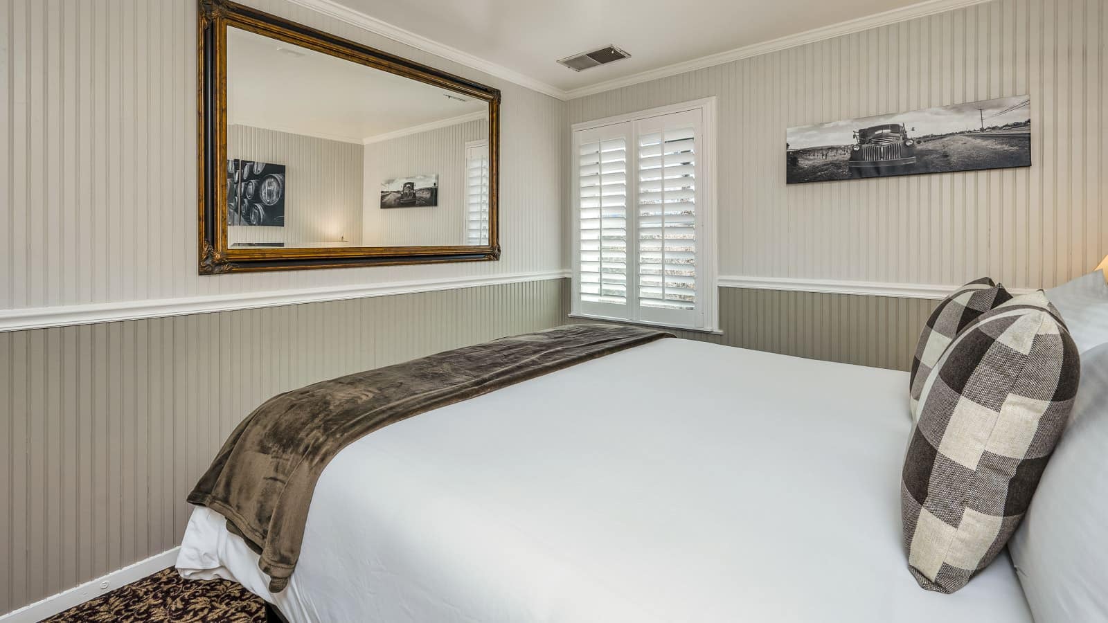 Bedroom with white walls, light gray wainscotting, floral carpeting, white bedding, and large framed mirror