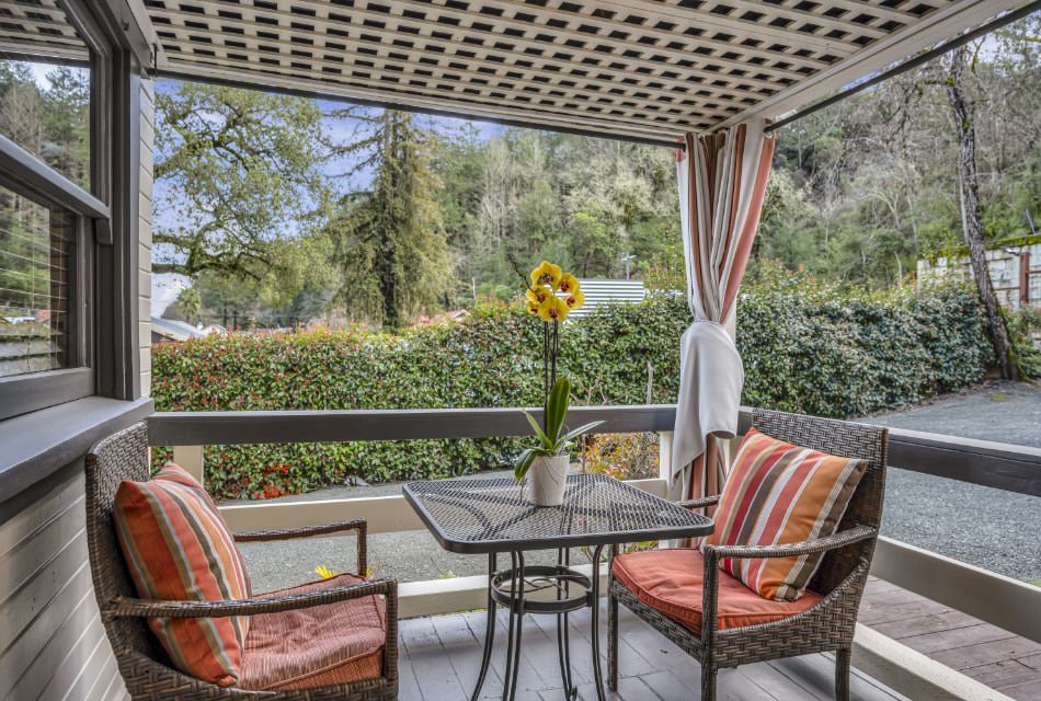 Exterior view of property's back covered porch with wicker patio furniture and green vegetation in the background