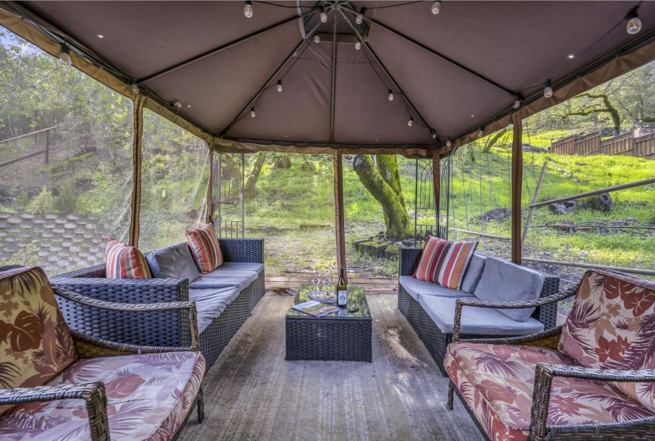 Gazebo draped with bug screens with gray wicker patio furniture