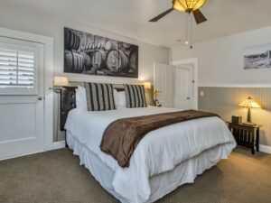 Bedroom with white walls, light gray wainscotting, light colored carpeting, white bedding, and dark wooden nightstands
