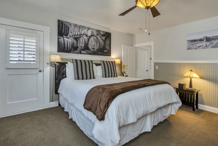 Bedroom with white walls, light gray wainscotting, light colored carpeting, white bedding, and dark wooden nightstands